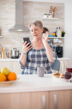Retired woman waves hello during a video conference from home, showing senior communication, digital connection and family contact.