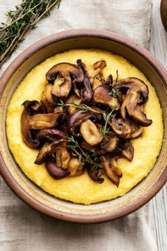 Rustic ceramic bowl with creamy cornmeal polenta, saut&eacute;ed mushrooms, and fresh thyme, on a linen cloth