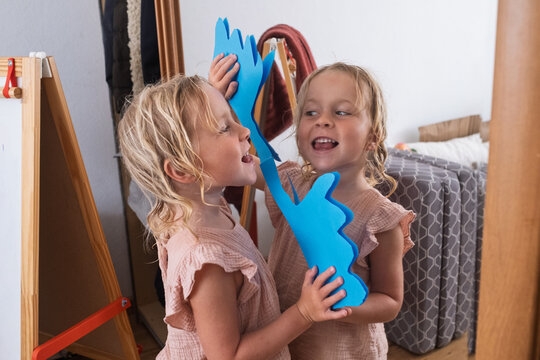 girl holding a handmade blue paper crown while looking at her reflection in a mirror.