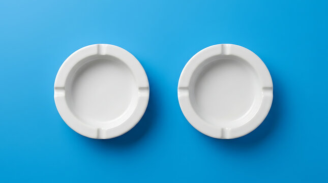 Two Clean White Ceramic Ashtrays with Four Notches Placed on a Vibrant Blue Background Studio Shot
