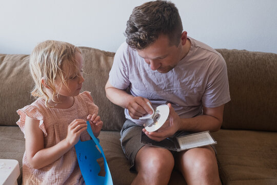 Father and his curious little daughter sitting on a couch while the man cleans a compact disc 
