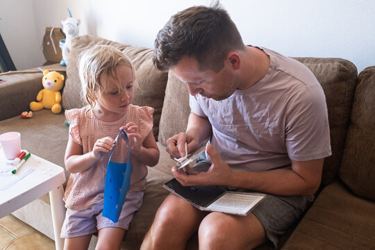 Father and his curious little daughter sitting on a couch while the man cleans a compact disc 