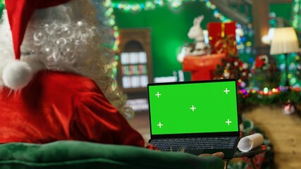 Obraz premium Santa Claus types on a green screen laptop while responding online to children's gift requests and asking what they want for Christmas.