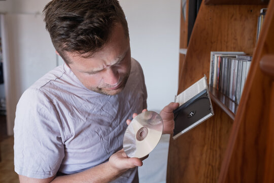 Man holding a compact disc near a bookshelf. 