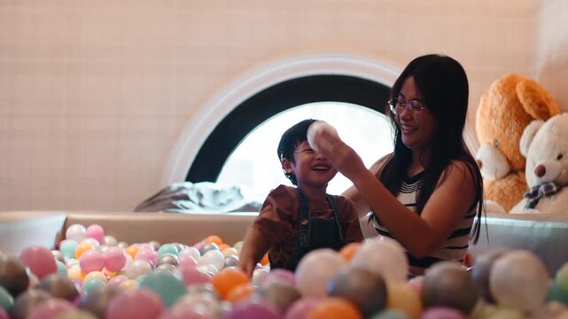 Happy mother and son playing and laughing in a ball pit at home