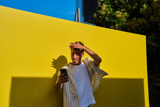 Young man enjoying smartphone content against yellow wall