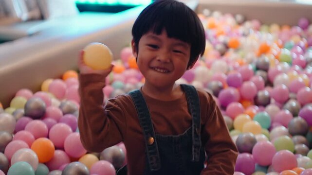 Happy young boy having fun inside a colorful ball pit at a playground
