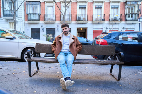 Young man relaxing on city bench in winter jacket