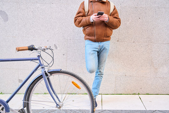 Courier person checking smartphone resting on city wall