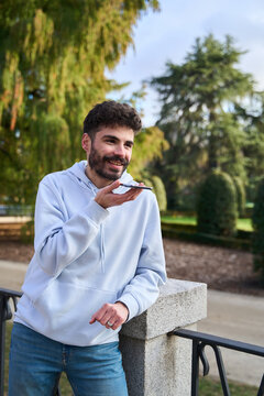 Young man sending voice message smartphone in park