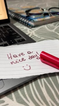 A hand leaving a note with good wishes and a smile on the desk. 24fps vertical video.