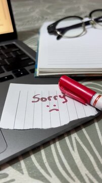 A hand leaving a note with a "sorry" message on a table. 24fps vertical video.