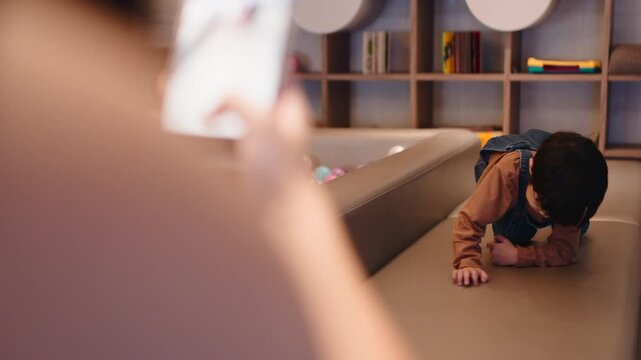 Mother filming her happy young son crawling and playing on a smartphone