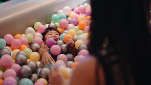Happy young kid having fun with mom inside a colorful ball pit