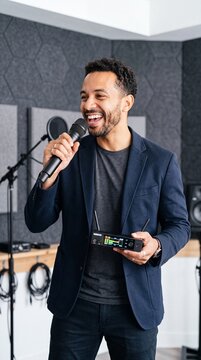 Smiling male podcaster or presenter holding a microphone and wireless audio receiver in a modern recording studio