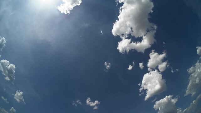 Timelapse looking straight up into a blue sky with cumulus clouds floating across a wide angle frame. The sun is peaking into the edge of the picture
