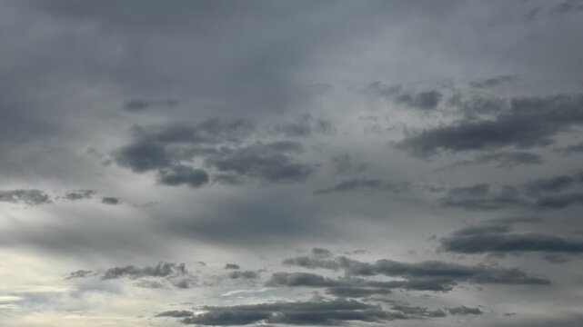 Timelapse of dramatic gray clouds floating through a sky with thin overcast clouds
