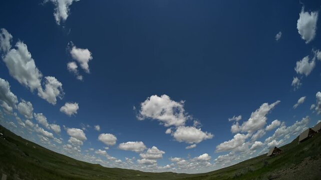 Timelapse fish-eye view of summer white cumulus clouds drifting through a blue sky with camping tents in the prairie foreground
