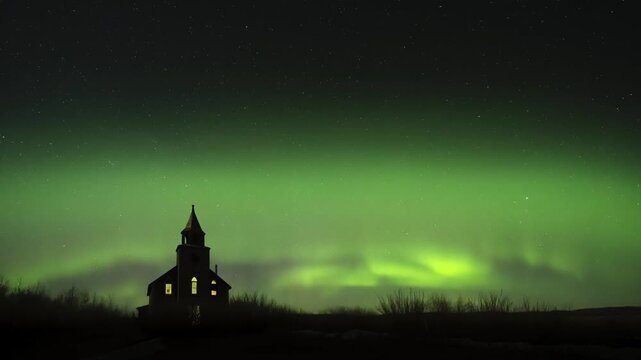 Timelapse of bright green aurora northern lights dancing behind an illuminated abandoned church. The sky is full of stars.
