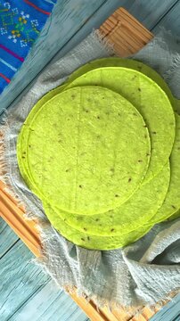Overhead view of raw nopal pads in clay bowl and green cactus tortillas on wooden table
