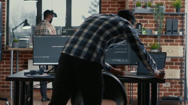 Software developer codes on a laptop in a software agency office, reviewing source code, data systems and application development tasks