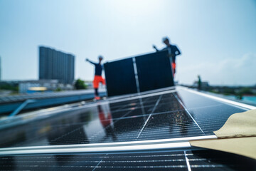 A renewable energy specialist in reflective workwear and helmet efficiently walks a module upright along the high roof line on the sweeping metal roof of a manufacturing plant in Southeast. © ultramansk