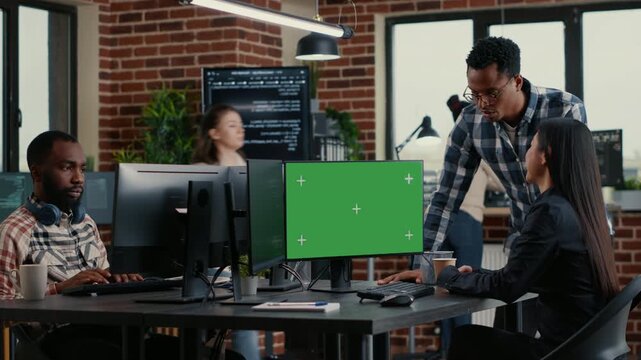 Two software developers review programming work beside a replaceable monitor display, connecting code analysis, mockup editing and office teamwork, inside a clean IT office.