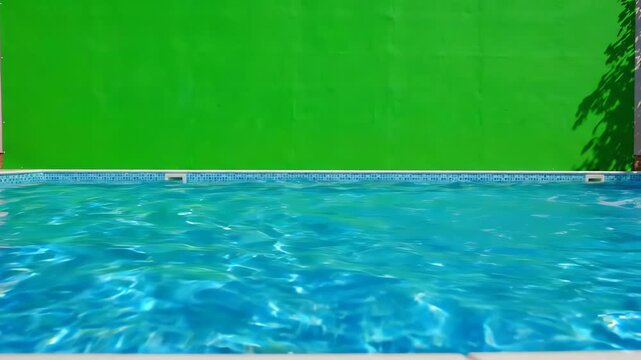 Camera panning over sparkling blue swimming pool water with a large chroma key green screen background for visual effects compositing