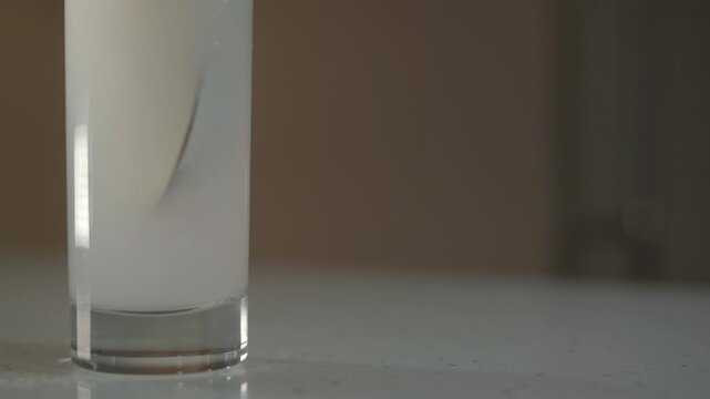 A teaspoon stirs powdered milk into a glass of water to prepare milk.