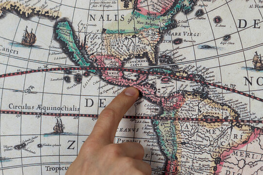 Close up to a male hand pointing with his index finger to the central american continent into a modern printed reproduction of a 17th century map