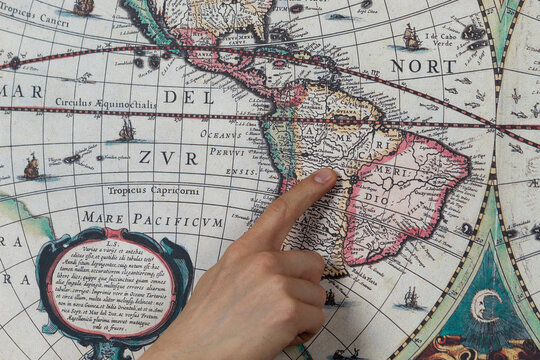 Close up to a male hand pointing with his index finger to the south american continent into a modern printed reproduction of a 1630 map