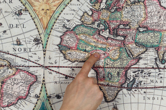 Close up to a male hand pointing with his index finger to the african continent into a modern printed reproduction of a 1630 map