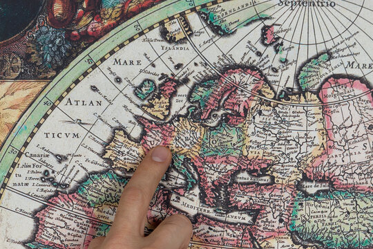 Close up to a male hand pointing with his index finger to the european continent into a modern printed reproduction of a 1630 map