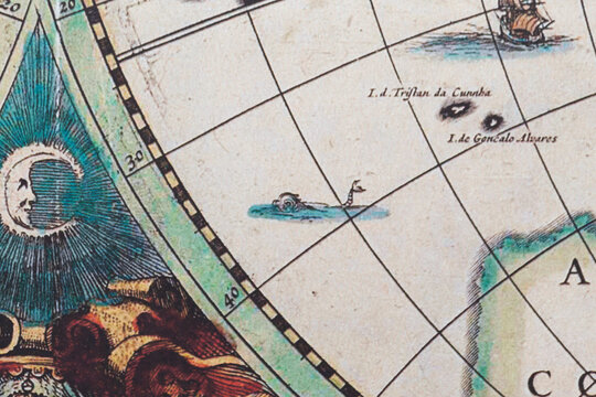Close up of a modern printed reproduction of a 17th century map showing an allegoric representation of sea creature and vintage maritime routes with galleons