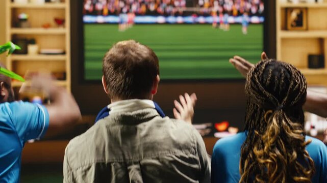 Joyous football supporters do a high five at home while celebrating a scored goal as thrilled soccer fans cheer after the team wins a tournament match.