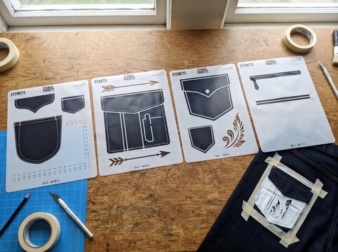 Set of plastic stencils for decorating denim pocket on wooden table. Tailor applying creative design to clothing. DIY fashion project, craft hobby and handicraft accessory concept.