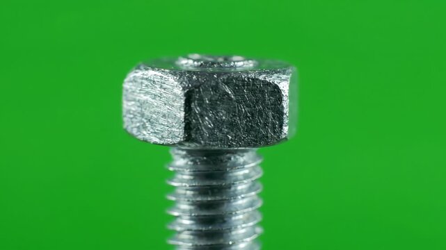 Close up of a metallic steel hex bolt rotating slowly against a bright green screen background for easy keying