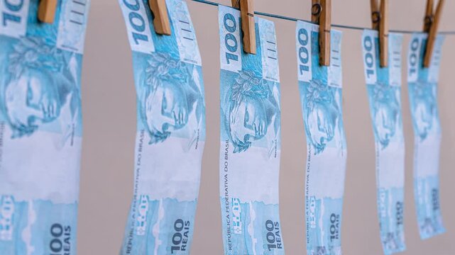 Brazilian one hundred real banknotes hanging on a clothesline with clothespins, symbolizing money laundering, corruption, financial crime, illegal wealth, tax evasion, bribery, fraud, and dirty money.