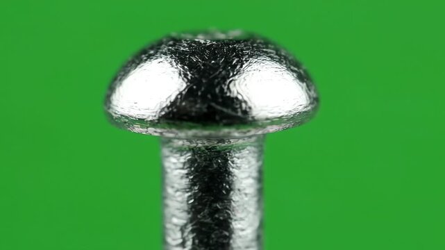 Close up shot of a metallic solid rivet rotating slowly against a bright green screen background for easy keying