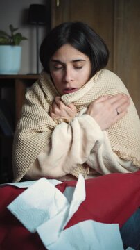 Young Latina woman sitting sick on her sofa at home. Health and wellness lifestyle video representing illness, recovery, self-care, home care, rest and seasonal flu symptoms.
