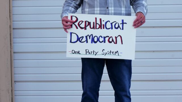 Demonstrator holds a handmade sign reading Republicrat Democran One Party System protesting corporate influence political duopoly elections and choice