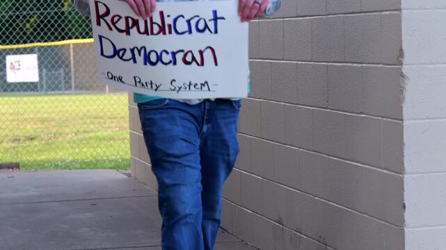 Demonstrator holds a handmade sign reading Republicrat Democran One Party System protesting corporate influence political duopoly elections and choice