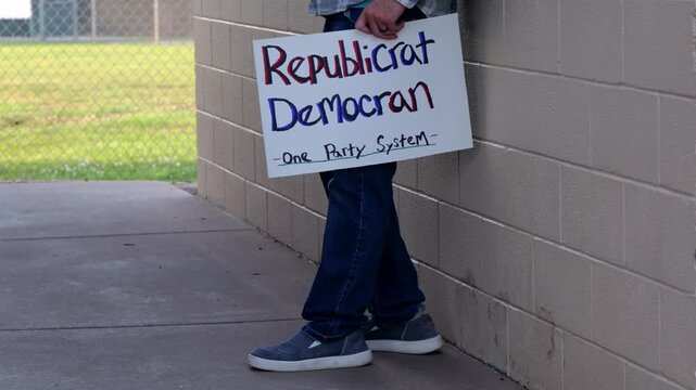 Demonstrator holds a handmade sign reading Republicrat Democran One Party System protesting corporate influence political duopoly elections and choice