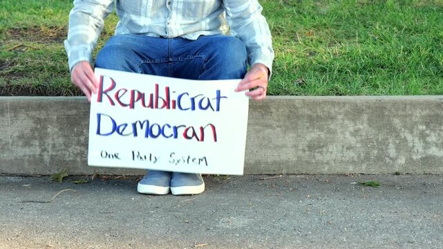 Demonstrator holds a handmade sign reading Republicrat Democran One Party System protesting corporate influence political duopoly elections and choice