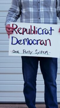 Demonstrator holds a handmade sign reading Republicrat Democran One Party System protesting corporate influence political duopoly elections and choice
