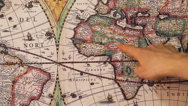 Detailed view of a male hand pointing with his index finger to a modern printed reproduction of a 17th century world map showing the African continent.