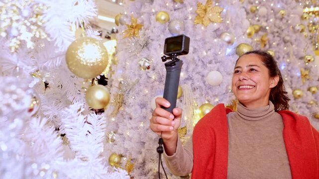 Influencer woman vlogging with an action camera near a white christmas tree