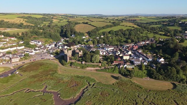 Aerial drone footage of the historic village of Laugharne in Carmarthenshire, Wales, featuring the River Coran estuary, traditional buildings, surrounding countryside and picturesque rural landscape 