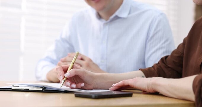 Insurance agent showing client where to sign document at table in office, closeup