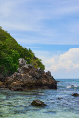 Obraz premium Tropical Rocky Coastline with Crystal Clear Sea and Lush Green Cliff Under Blue Sky